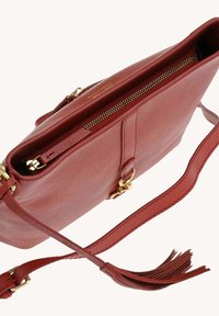 Sac en cuir texturé rouge en bandoulière avec fermeture éclair dorée, détail de boucle, bandoulière ajustable et accent en frange sur fond blanc.