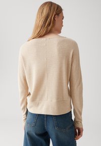 Maglietta a manica lunga beige chiaro con un design a maglia waffle testurizzata, caratterizzata da una vestibilità rilassata e cuciture delle spalle drop per facilitare il movimento.