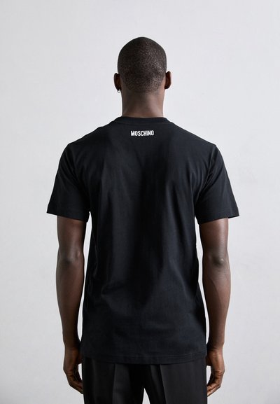 Must proovist t-särk, millel on ümar kaelus ja lühikesed varrukad. Ülemisel seljal on valge "MOSCHINO" logo trükitud. Sujuv tekstuur.