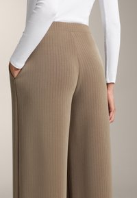 Béžové široké nohavice s rebrovanou textúrou a vysokým pásom, so bočnými vreckami a hladkým povrchom, skombinované s bielym topom s dlhým rukávom.