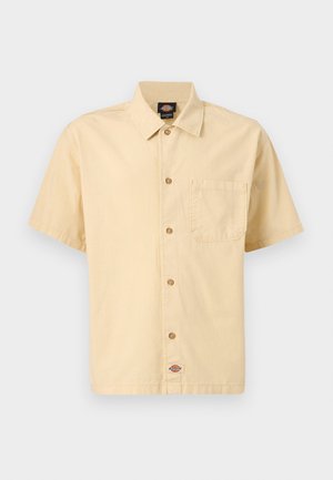 Camisa beige de manga corta con botones, cuello puntiagudo, bolsillo en el pecho a la izquierda y etiqueta con el logo de la marca en la parte inferior frontal.