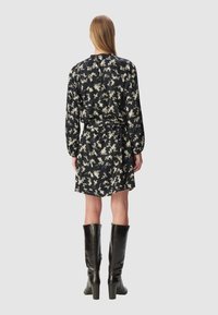 Czarna sukienka w kwiatowy wzór z długim rękawem, zawiązywana w talii i sięgająca powyżej kolan. Połączona z czarnymi, skórzanymi kozakami do ud na obcasie słupkowym.