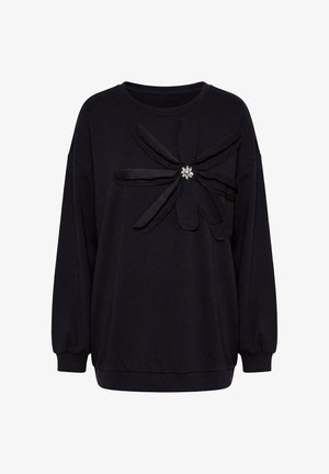 Czarna bluza z długim rękawem z dużą tkaninową kokardą oraz broszką w kształcie kwiatu z klejnotami umieszczoną na środku klatki piersiowej.