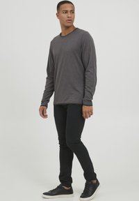 Maglietta grigia a maniche lunghe con scollo rotondo, abbinata a jeans skinny neri e sneaker nere. Design semplice con una texture liscia.