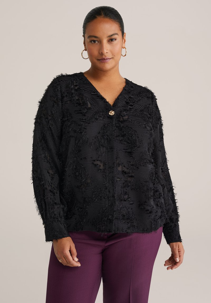 Blusa nera in tessuto testurizzato con scollatura a V, maniche lunghe e un abbellimento centrale. Progettata con dettagli sfilacciati in tutto il capo.