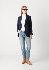 Navy striped blazer over a white turtleneck, paired with light blue jeans and tan ankle boots. Brown square sunglasses complete the look.