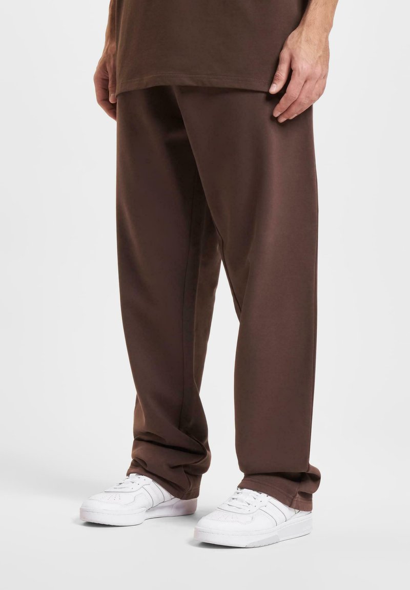 Pantalons marron à coupe décontractée en matériau doux, avec une texture lisse et des baskets blanches contrastantes pour un look décontracté.