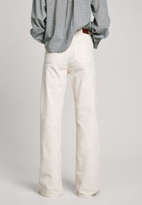 Jeans blancos de pierna ancha, elaborados en denim, con una cintura alta, textura ligeramente áspera y dos bolsillos traseros. El conjunto incluye una camisa a cuadros.