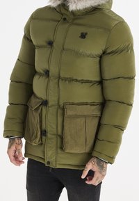 Puffjakke i mørk olivengrøn med hætte af kunstpels, sorte knapper og to store frontlommer med tekstureret finish.