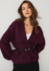 Pluche, diep paarse trui met een V-hals, lange mouwen en een taille met riem. Zachte textuur en losse pasvorm.