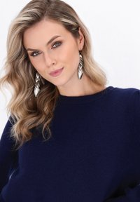 Silberne ohrringe in Blattform mit polierter Oberfläche, getragen mit einem navyblauen Pullover mit rundem Ausschnitt und strukturiertem Stoff.
