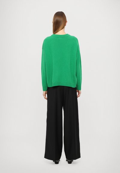 Green knit sweater with a relaxed fit, round neck, and dropped shoulders, paired with wide-leg black trousers. Smooth texture, minimal design.