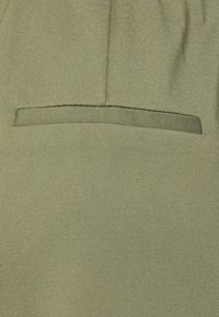 Close-up van olijfgroene stof met een horizontale sleufzak en een zichtbare naden erboven.