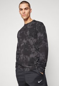 Long-sleeve black tie-dye shirt made of soft material, features ribbed neckline, and small Nike logo on the chest. Styled with dark sweatpants.