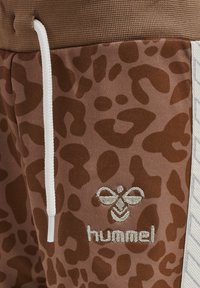 Bruine sportieve broek met een luipaardprint, een witte trekkoord en geborduurd logo langs het been, gemaakt van een gestructureerde stof.