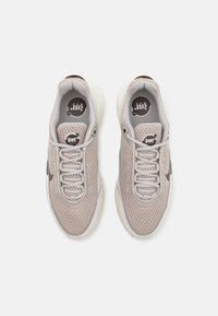 Grå nät sneakers med runt svart logotyp, tunna snören och vadderade vita sulor; har en texturerad ovandel och subtila svarta detaljer.