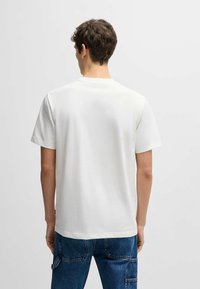 Hvid kortærmet t-shirt med rund halsudskæring, glat tekstur og en afslappet pasform, parret med blå denimbukser med lommer.