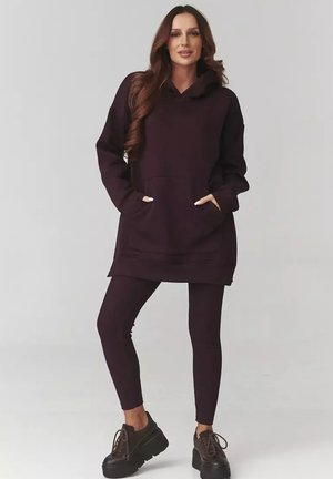 Fioletowy, oversize'owy hoodie z frontowymi kieszeniami, zestawiony z pasującymi legginsami. Teksturowany materiał, kaptur i luźny krój. Czarne buty na grubej podeszwie.