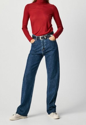 Haut rouge à manches longues côtelé, jeans en denim bleu foncé taille haute, lâches avec une ceinture noire, et baskets blanches. Tissu texturé visible.