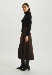 Haut à col roulé noir associé à une longue jupe marron. La jupe présente une texture lisse et arrive en dessous du genou, complétée par des bottes noires.