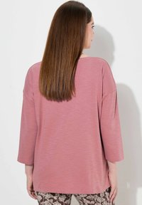 Rosa, locker sitzendes Oberteil mit 3/4-Ärmeln, aus einem weichen, leichten Stoff gefertigt. Verfügt über einen runden Ausschnitt und eine lässige Silhouette.