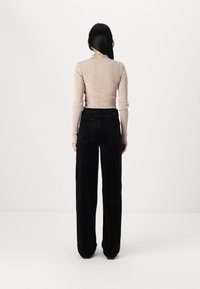 Haut beige à manches longues en côtelé avec un col volanté, associé à un pantalon large en velours côtelé noir taille haute. Détails de texture et de silhouette clairs.