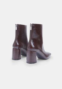 Brown leather ankle boots with a pointed toe, square heel, and a back zipper for closure, featuring a glossy finish and smooth texture.
