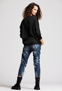 Schwarzer, übergroßer Pullover mit langen Ärmeln, kombiniert mit zerrissenen blauen Jeans und schwarzen Stiefeln. Einfaches Design mit lässigem Schnitt.