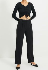 Czarny długi rękaw crop top z marszczeniami z przodu, połączony z czarnymi spodniami o wysokim stanie i prostymi nogawkami oraz czarnymi szpilkami.