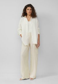 Crème oversized shirt, witte tanktop en wijde cargobroek. Getextureerde stoffen, knoopsluiting en zijzakken op de broek.