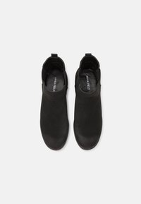 Svarta ankelboots i glatt material med rundad tå, elastiska sidopaneler och dragflik för enkel på- och avtagning.