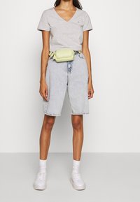 Grå v-ringad t-shirt, ljusa tvättade denimshorts och vita sneakers. En liten gul midjeväska bärs i midjan och ger en färgklick.