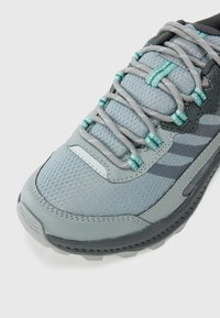 Gray athletic shoe featuring a mesh upper with turquoise accents, textured panels, and a black rubber outsole, designed for outdoor activity.