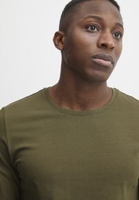Olijfgroen, aansluitend t-shirt met ronde hals van zachte katoen. Beschikt over korte mouwen en een gladde, gelijkmatige textuur zonder zichtbare patronen.