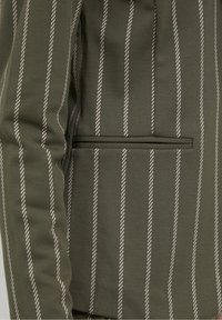 Tissu vert avec fines rayures blanches verticales. Présente une coupe ajustée et une poche passepoilée. Texture lisse avec une apparence sur mesure.