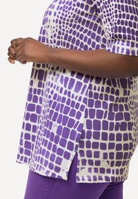 Top morado con estampado y mangas cortas, presenta un diseño de cuadrícula sobre un fondo claro. Las aberturas laterales mejoran el movimiento; tejido ligero.
