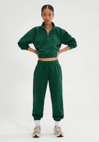 Sudadera verde corta con cuello de cremallera, combinada con joggers a juego que cuentan con una cinturilla elástica y tobillos ajustados. Detalle textural ligero.