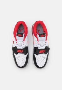 Zapatillas en blanco y negro con acentos rojos, con una parte superior texturizada, caja de dedos perforada y una correa distintiva etiquetada como "NIKE".