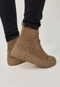 Taupe Wildleder-Ankle-Boots mit Schnürdesign, strukturiertem Gummisole und dicker Plattform für zusätzlichen Höhengewinn. Sichtbare Steppnähte an den Seiten.