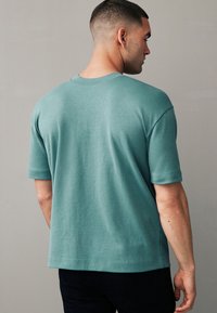Hellblaues T-Shirt mit kurzen Ärmeln, entspannter Passform, runder Ausschnitt und sichtbaren Nähten am Saum. Glatte, weiche Stofftextur.