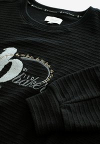 Schwarzer gerippter Pullover mit gesticktem Logo in Silber und Gold. Rundhalsausschnitt und strukturiertes Gewebe mit langen Ärmeln.