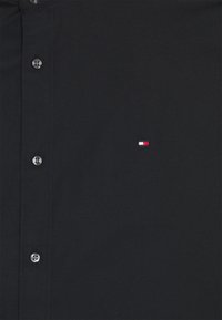 Czarna koszula na guziki wykonana z gładkiej tkaniny, z klasycznym kołnierzykiem, wyposażona w srebrne guziki oraz małe, wielokolorowe logo na piersi.