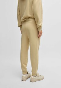Beige sweatpants met een taps toelopende pijp, elastische tailleband en boorden. Gepaard met lichtbeige sneakers. Zachte, textuurstof.