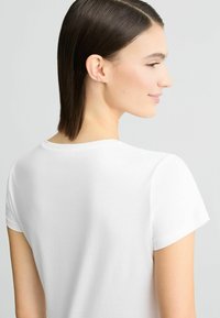 T-shirt blanc à manches courtes avec un col rond, texture douce, design simple et sans motifs visibles, vue de dos.