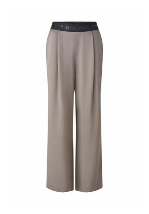Beige weite Hosen mit einem schwarzen elastischen Bund, der ein sich wiederholendes Logo trägt. Hergestellt aus glattem Stoff mit Plissee-Details.