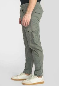 Olijfgroene cargobroek met meerdere zakken, een slim fit en verstevigde stiksels. Gecombineerd met witte sneakers.