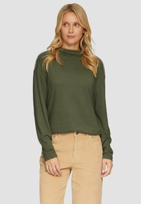 Olijfgroene lange mouw top met een hoge hals en gedetailleerde stiksels langs de schouders, gecombineerd met beige corduroy broek.
