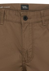 Bruine textuurbroek taille met zwarte knoop, lussen voor riem en "camel active" merklabel aan de binnenkant van de tailleband.