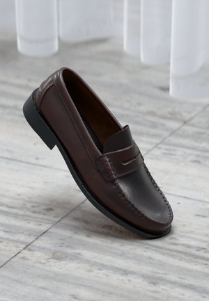 Loafer de couro castanho com um acabamento liso, bico arredondado, detalhes costurados e uma sola preta brilhante baixa. Adequado para uso formal ou casual.