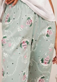 Světle zelené pyžamové kalhoty s veselým potiskem růžových domků a stromů uvnitř kruhových ozdob, s bílými mašlemi a hvězdami. Měkká bavlněná látka.